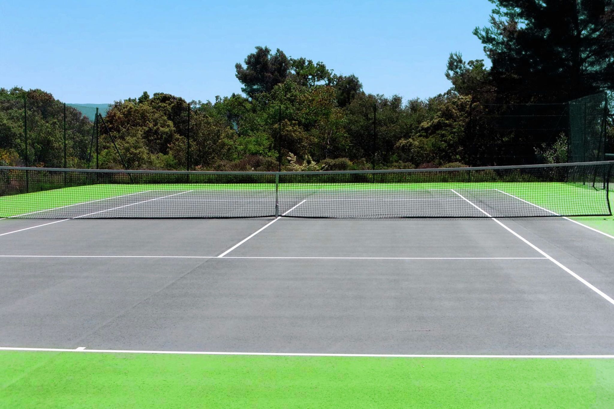 A tennis court with a net, surrounded by trees and a clear sky.