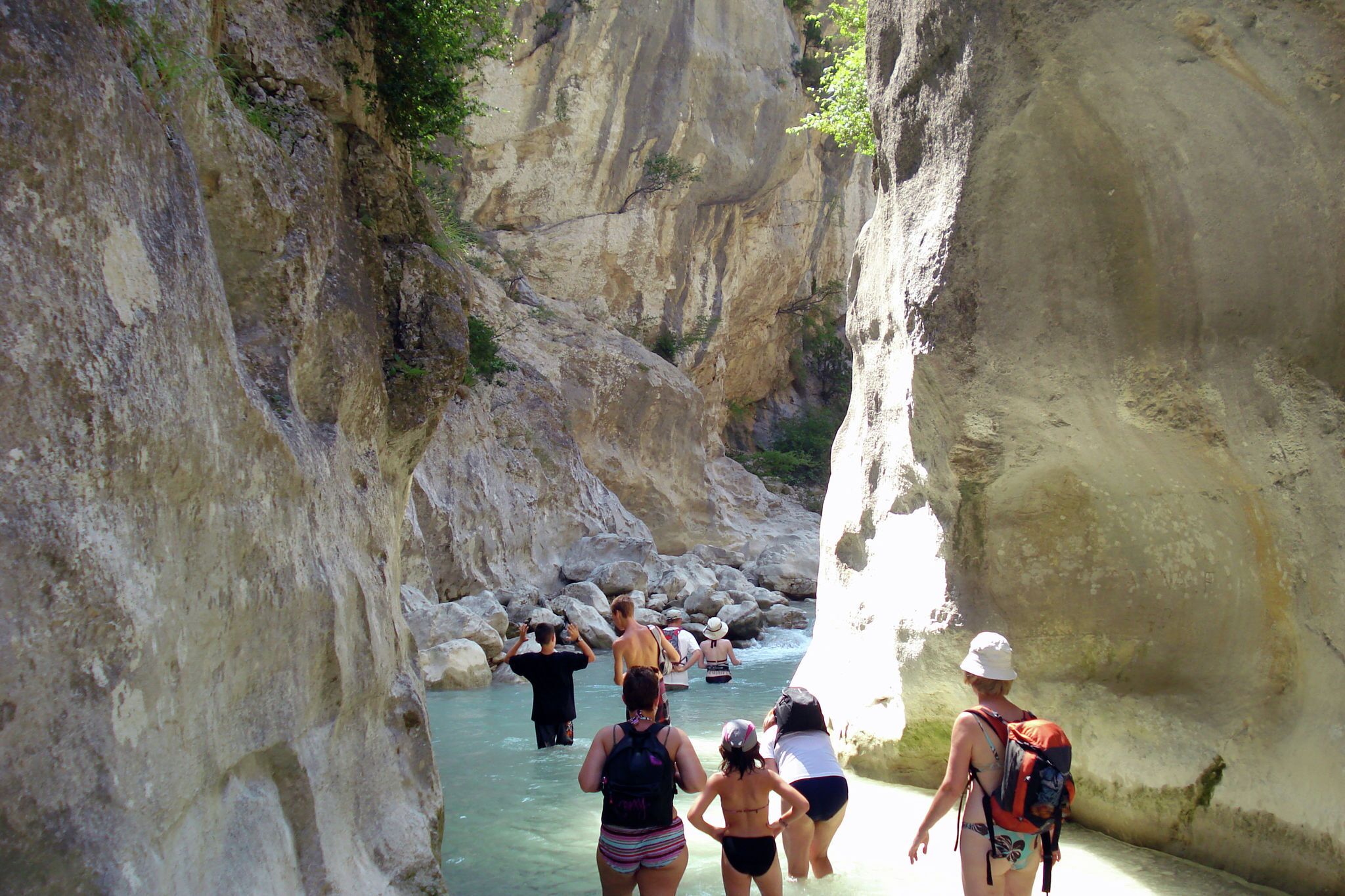 Un gruppo di persone cammina attraverso un canyon stretto con pareti rocciose e un ruscello di acqua limpida.