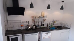 Una cocina compacta equipada con microondas, tostadora, hervidor y lavavajillas. Hay luces colgantes, un lavabo y una repisa con vajilla.