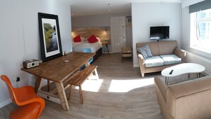 Una sala moderna con una mesa de comedor de madera, un sofá, un televisor y una cama con cabecera de madera.
