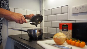 Una cocina con una persona cocinando, una tabla de cortar con verduras y una caja de arroz.