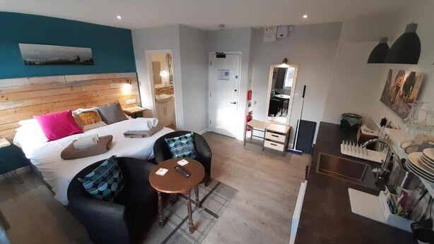 Una habitación de hotel con cama, sofá, una mesita, escritorio, espejo, armario y kitchenette.
