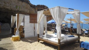 A beach cabana with a wooden bed and white canopy, surrounded by beach chairs and umbrellas. - sunny ap. for 2-6 people, exclusive 1a location directly on the beach by the sea (Ferragudo)