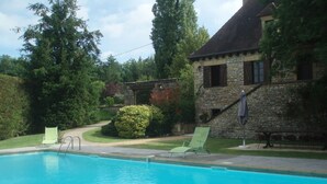 Ein Schwimmbecken mit zwei Liegestühlen und einem Steinhaus im Hintergrund.