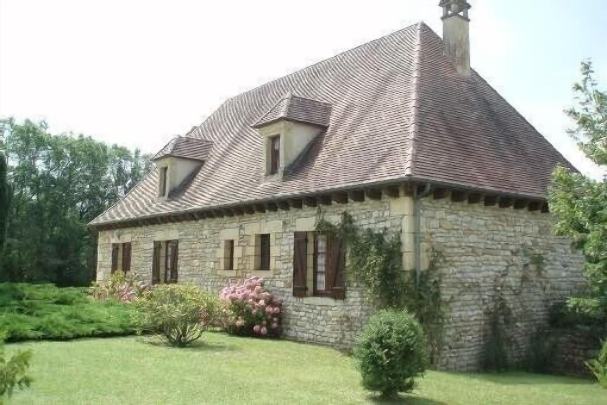A stone house with a pitched roof, a chimney, and a small garden with pink flowers.