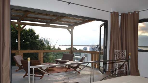 En balkon med fletstole og en seng, med udsigt over vandet.
