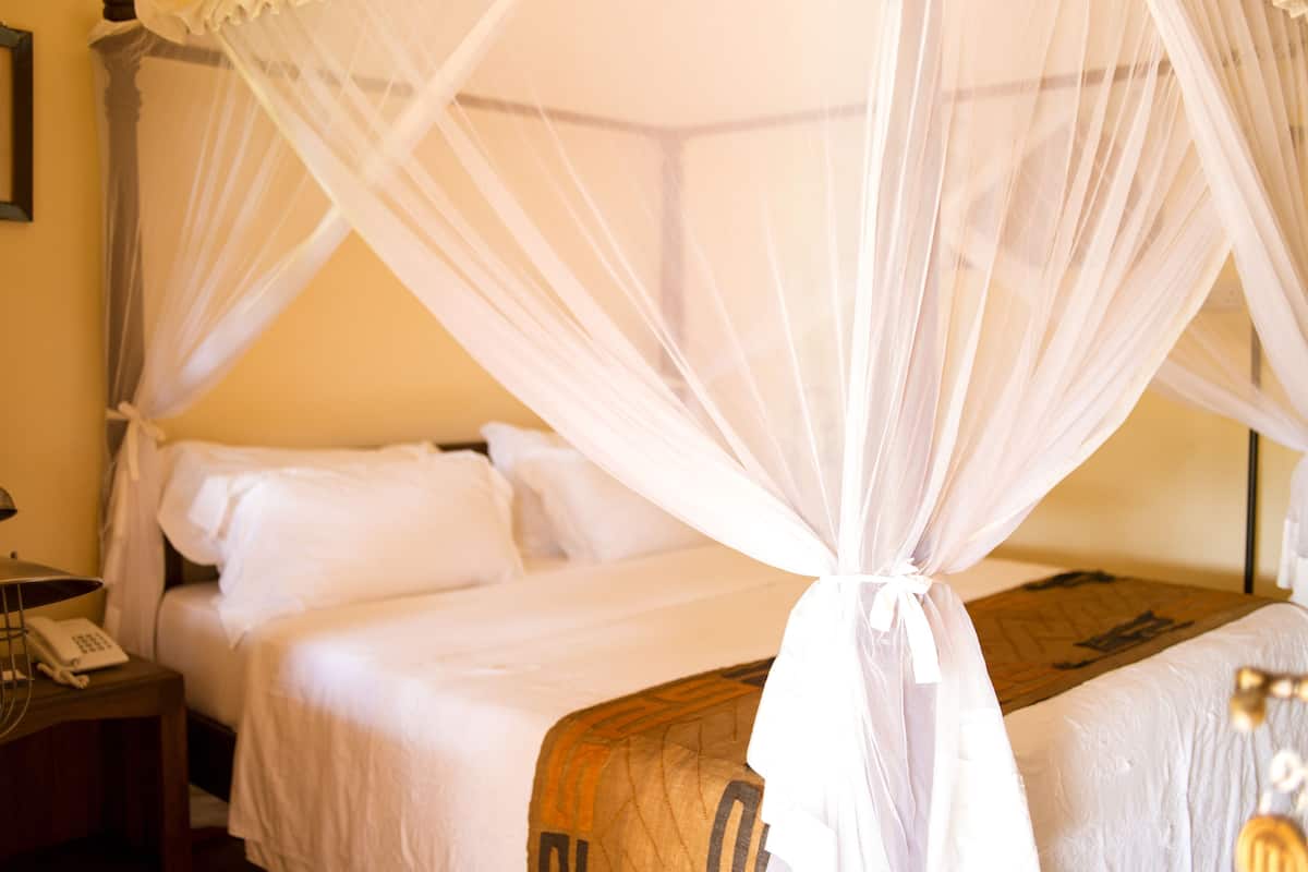 Een bed met hemelbed, een nachtkastje met telefoon en een wandlamp.