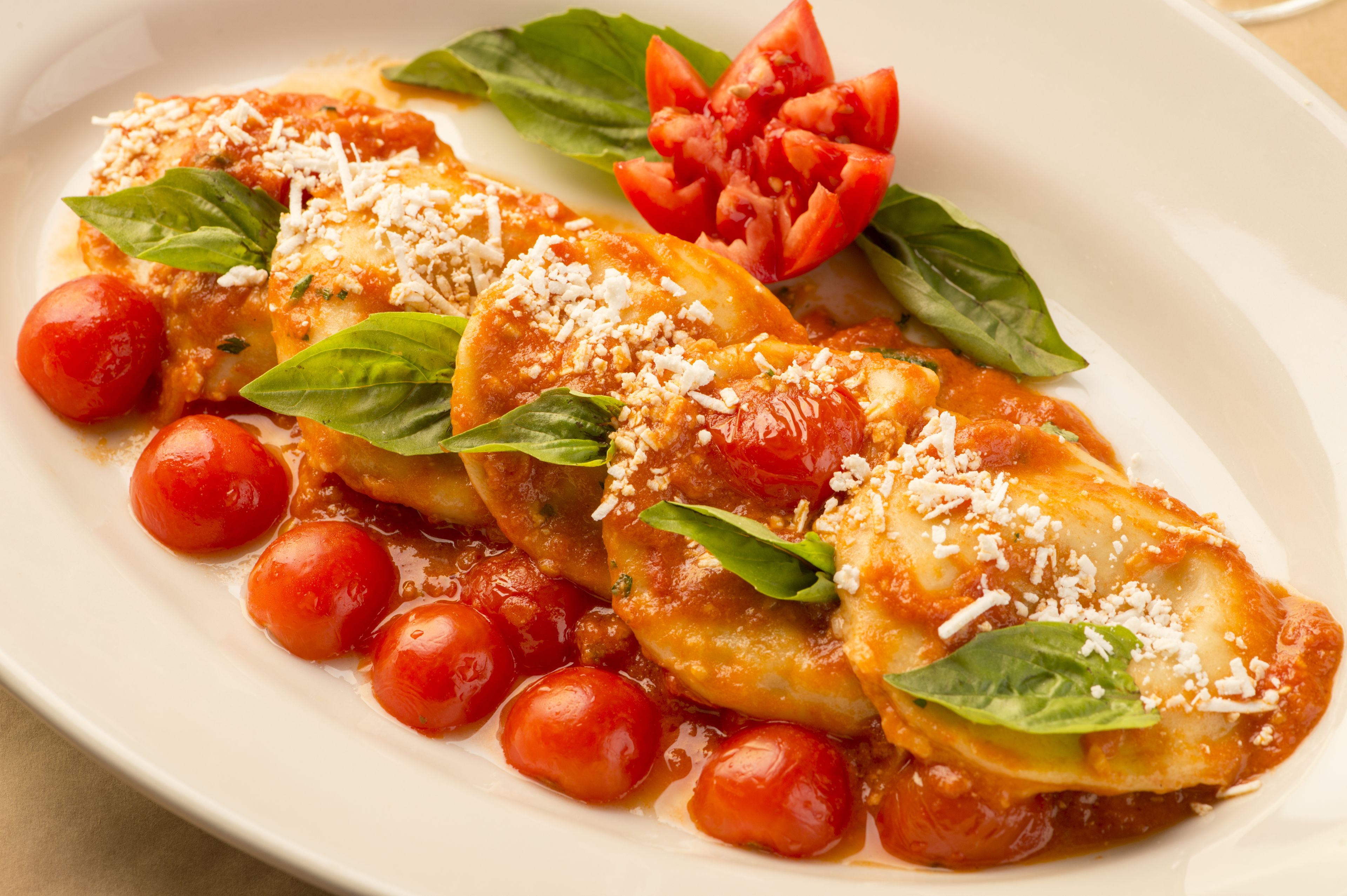A plate of stuffed pasta with tomato sauce, garnished with basil and cherry tomatoes.