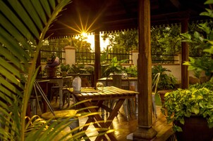 Een terras buiten met houten tafels en stoelen, omgeven door plantenpotten en een hek.