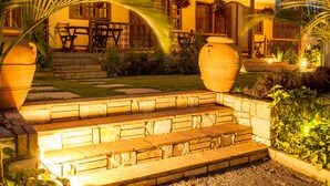 A well-lit outdoor patio area with stone steps leading to a covered seating area, surrounded by lush greenery and large planters. - Villa Kololo Guest House (Kampala)