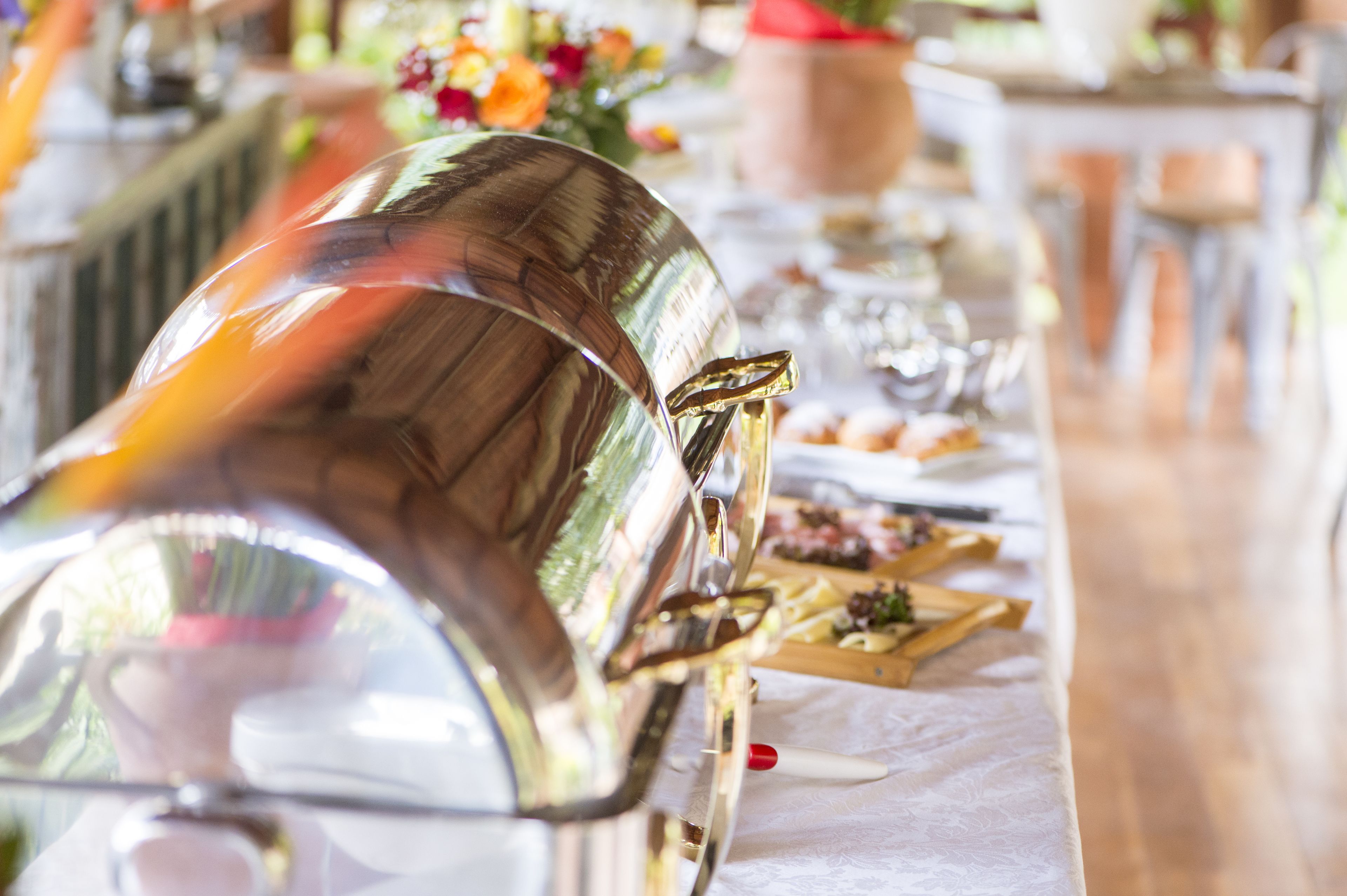 Montaje de bufé con una gran fuente plateada, una tabla de madera con alimentos y un mantel blanco.