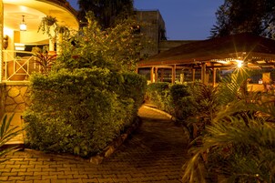 Un camino pavimentado que conduce a un espacio exterior cubierto con plantas y un edificio al fondo.