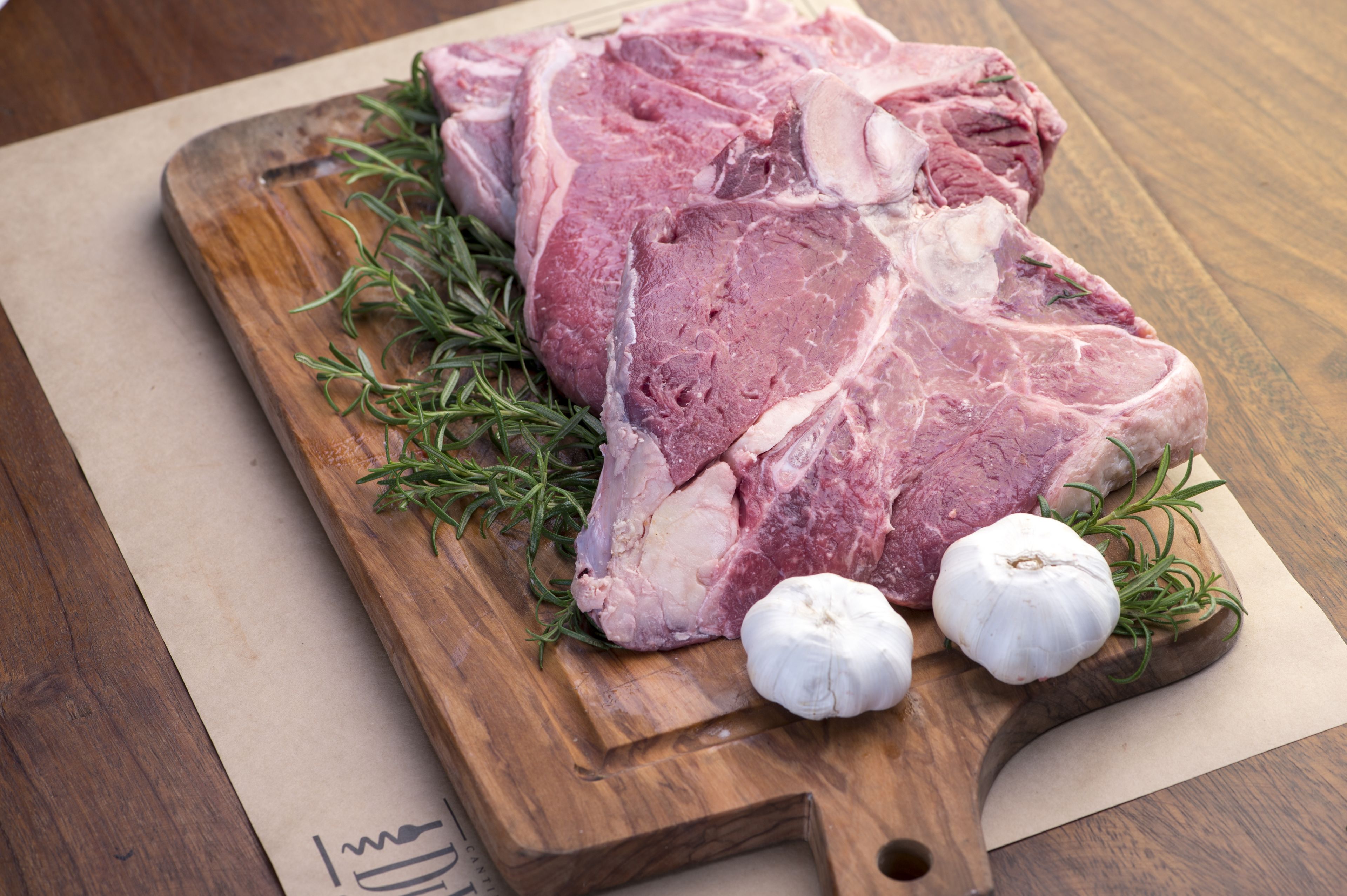 A raw pork chop on a wooden cutting board with rosemary and garlic cloves.