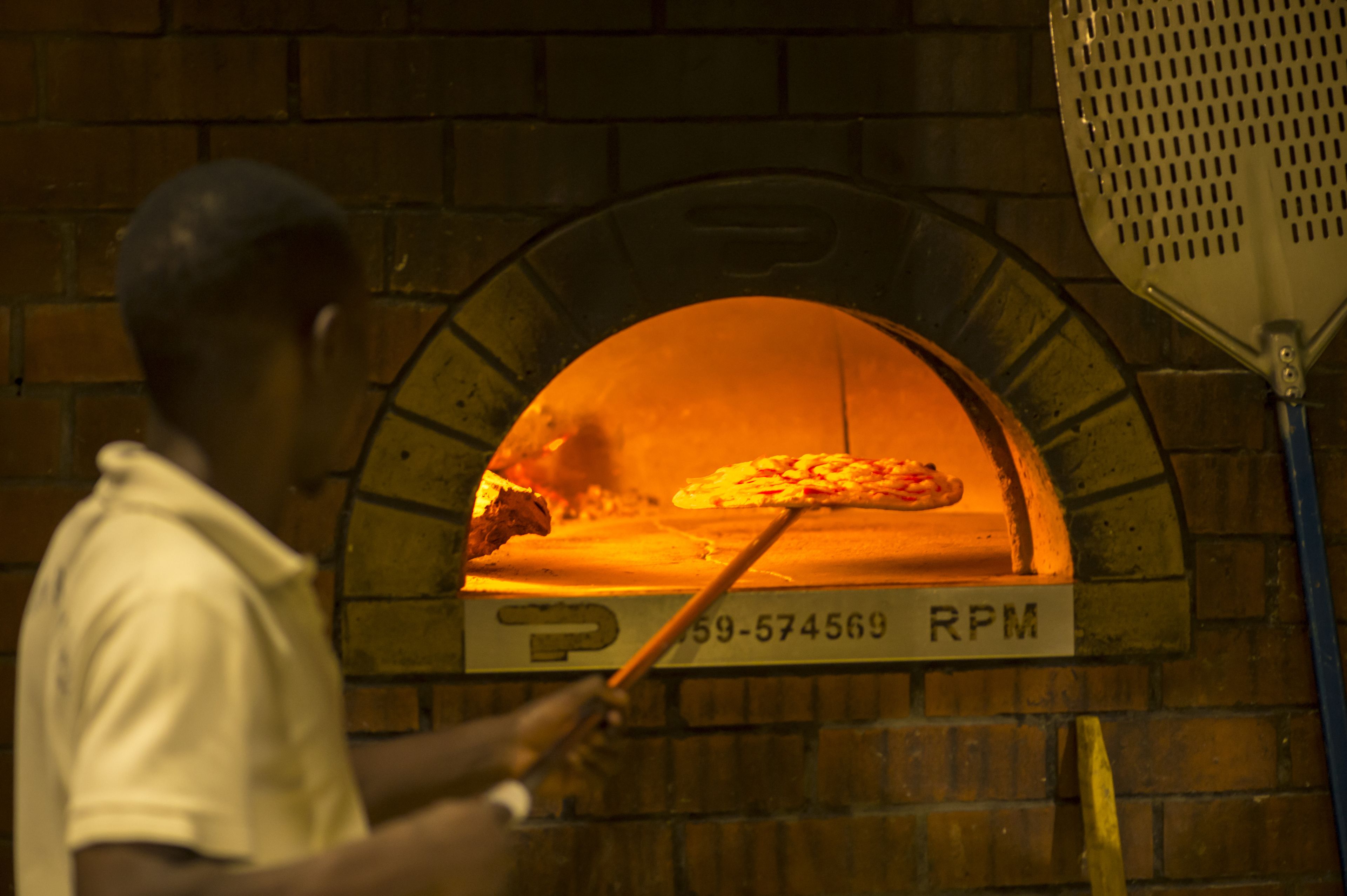 Une personne utilise une pelle à pizza pour sortir une pizza d’un four en briques.