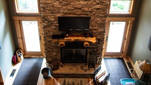 A stone fireplace with a television, a wooden bench, and a wreath above it.