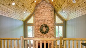 A cozy room with a stone fireplace, wooden beams, and a wooden railing.