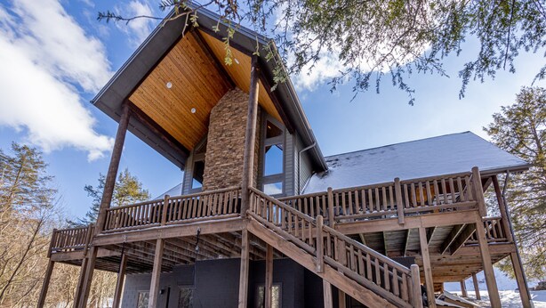 A wooden cabin with a large chimney, a deck, and a staircase leading to the upper level.