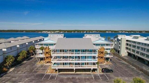 Un hotel con un edificio central de grandes ventanales y techo plano, rodeado de estacionamiento y vista al mar.