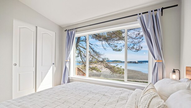 A bedroom with a large window overlooking a beach and a distant view of a bridge. - Unique Waterfront Beach House, 1 mile from Friday Harbor (Friday Harbor)