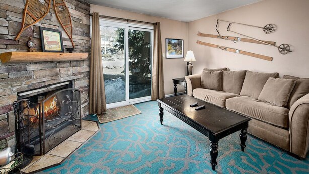 A cozy living room with a fireplace, a sofa, a coffee table, and a view through a sliding glass door.