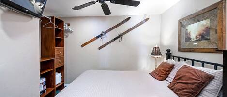 Un dormitorio con cama, ventilador de techo, televisión montada en la pared y esquíes colgados.