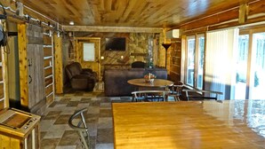 A rustic cabin interior with a wooden dining table, a sofa, and a television mounted on a stone wall. - Peninsula Lodge Fish Creek (Gibraltar)
