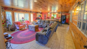 A spacious living room with a large sectional sofa, a coffee table, and a fireplace. The room has wooden walls and a tiled floor. - Peninsula Lodge Fish Creek (Gibraltar)