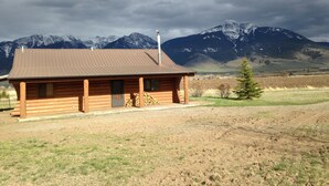 A wooden cabin with a metal roof, situated in a rural area with a mountain range in the background. - Peaceful, Mountain Setting.  Yellowstone Country. (Livingston)