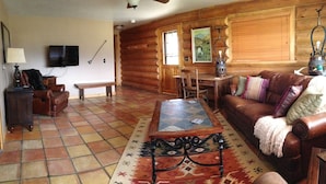 A cozy log cabin interior with a wooden dining table, leather sofa, and a patterned rug. - Peaceful, Mountain Setting.  Yellowstone Country. (Livingston)