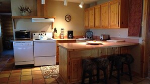A kitchen with wooden cabinets, a microwave, a coffee maker, and a toaster. There are two stools at the island. - Peaceful, Mountain Setting.  Yellowstone Country. (Livingston)