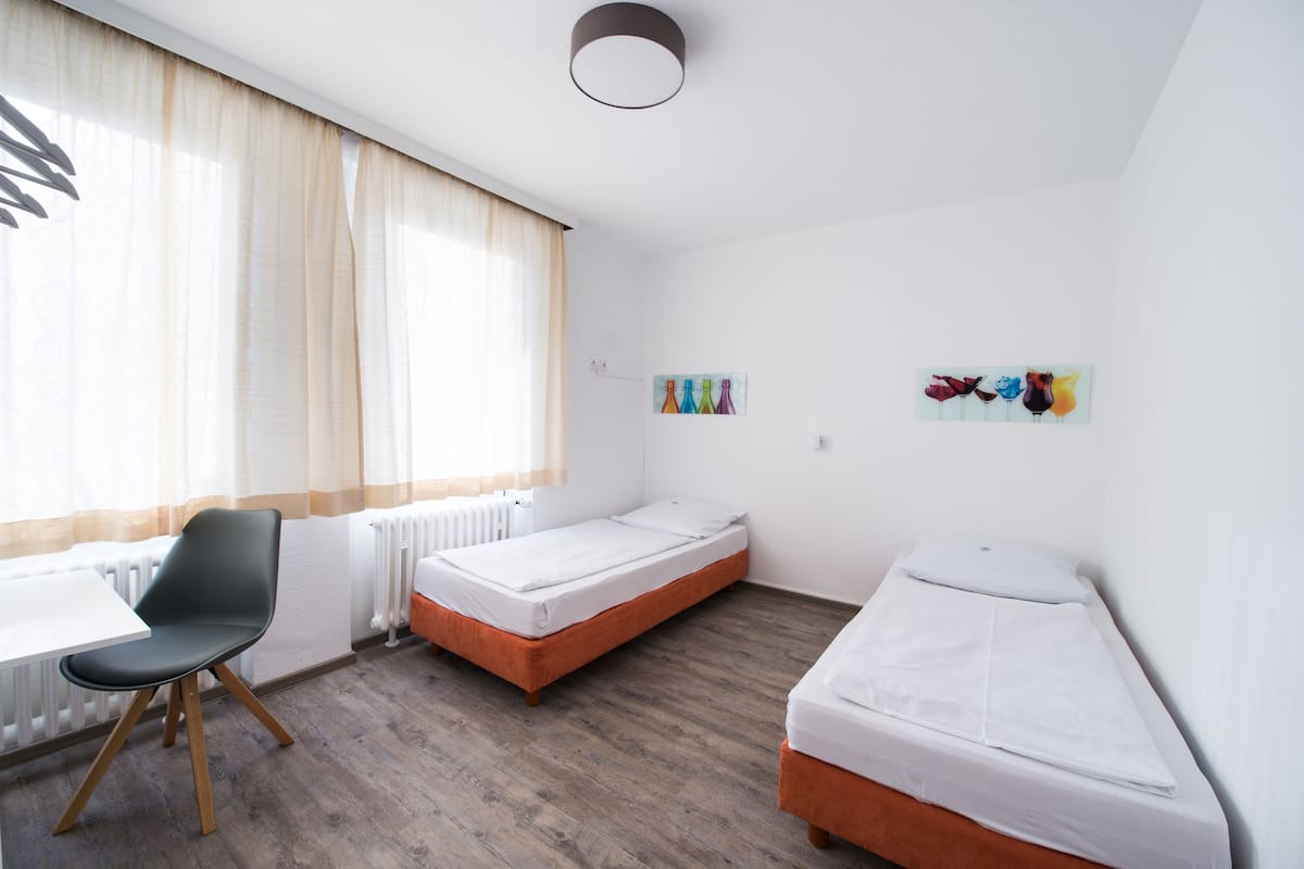 Quarto com duas camas de solteiro, uma mesa, uma cadeira e um radiador.