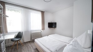 A hotel room with a bed, a desk, a chair, a TV, and a window with curtains. - SOVA Hotel (Kassel)