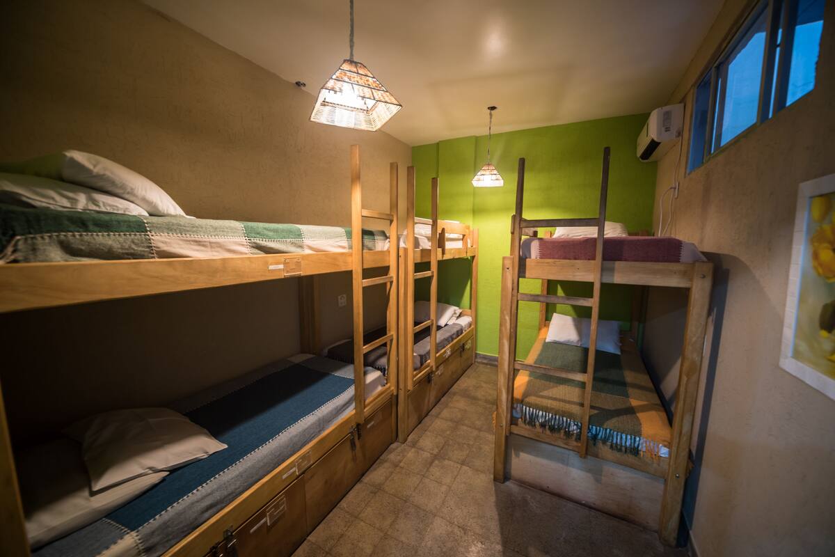A dormitory room with bunk beds, a small desk, and a window.