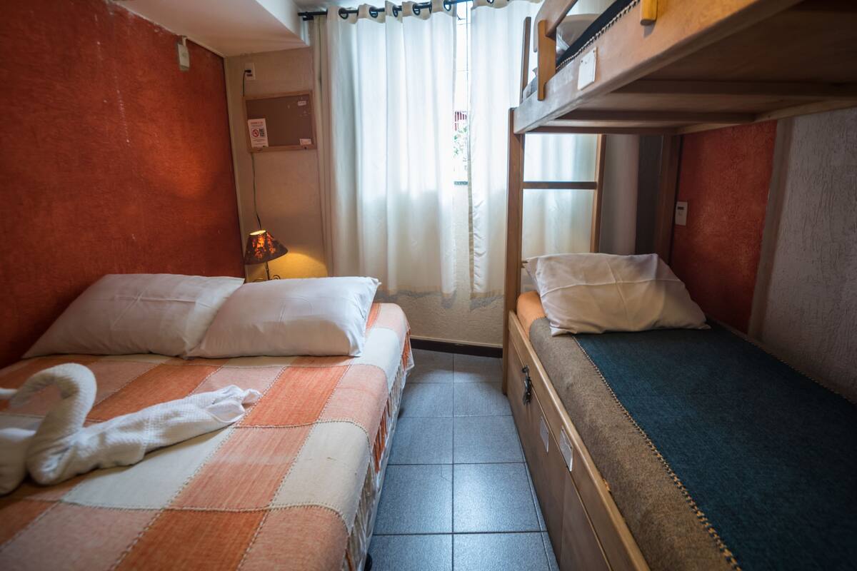 A compact room with two beds, a small table, and a window with curtains.