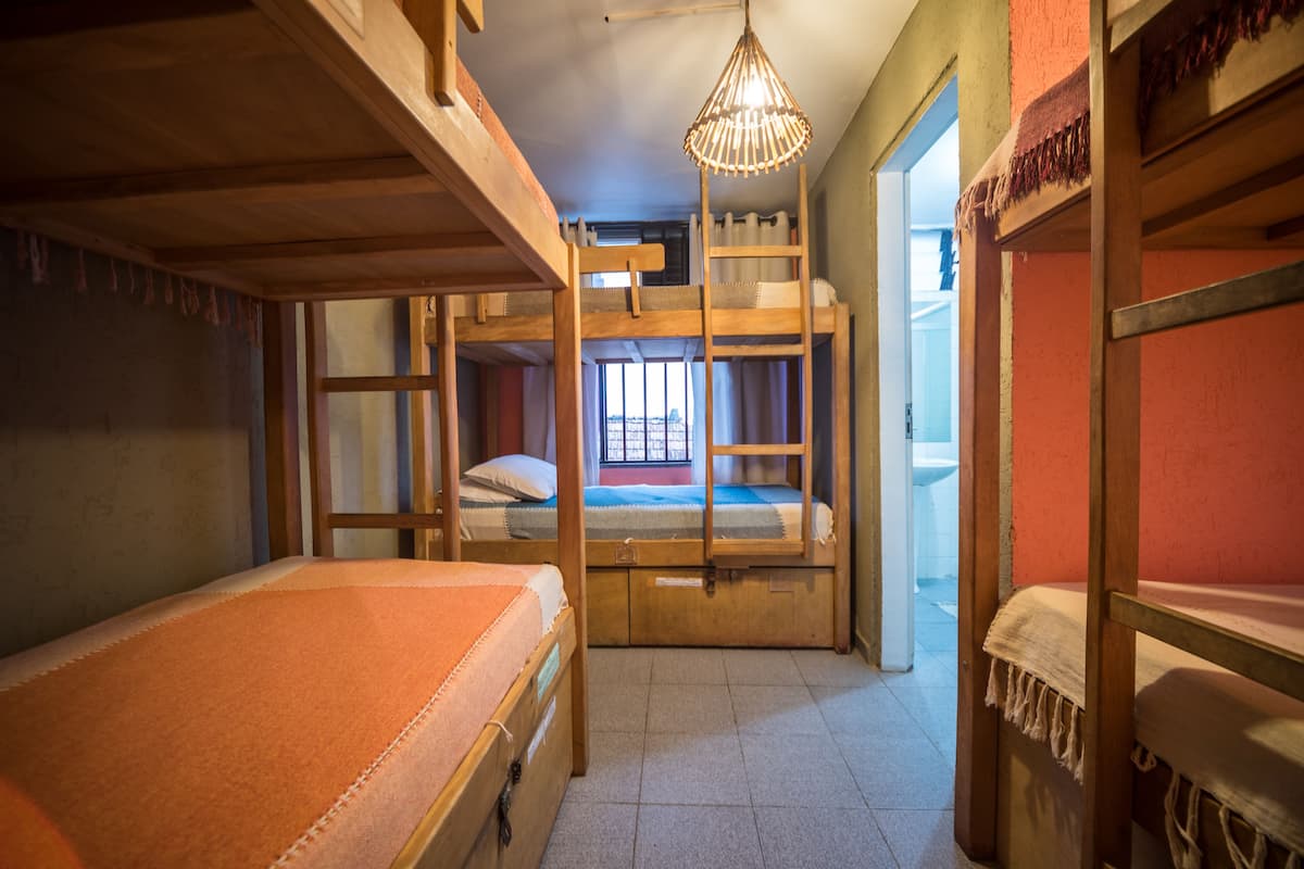 A dormitory room with bunk beds, a window, and a hanging light fixture.