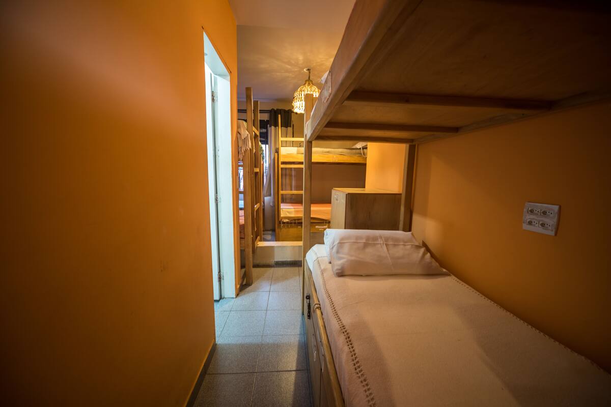 A narrow hallway with a bunk bed on the right, a wooden door on the left, and a staircase leading to another room.
