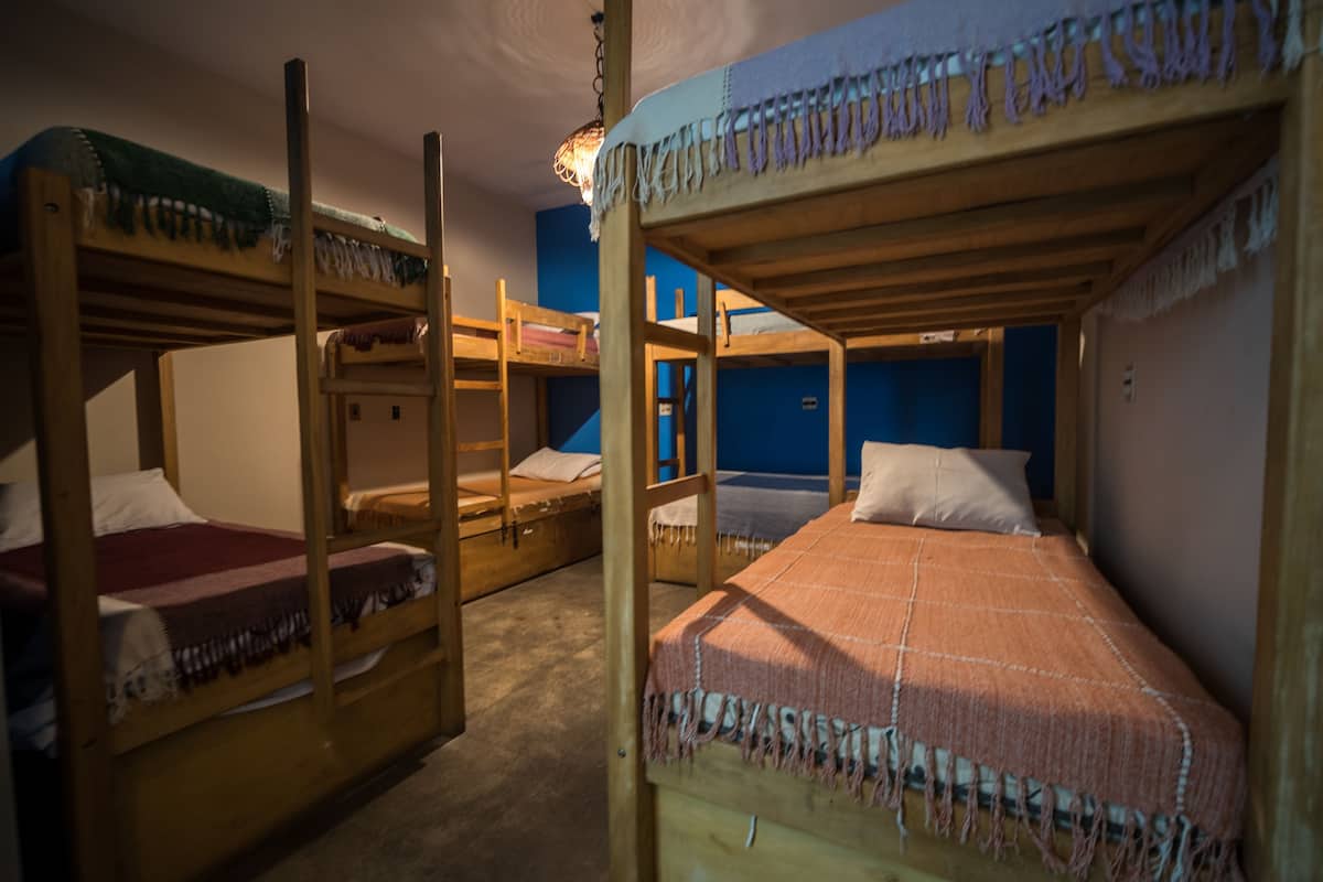 A dormitory room with bunk beds, a blue wall, and a ceiling light fixture.