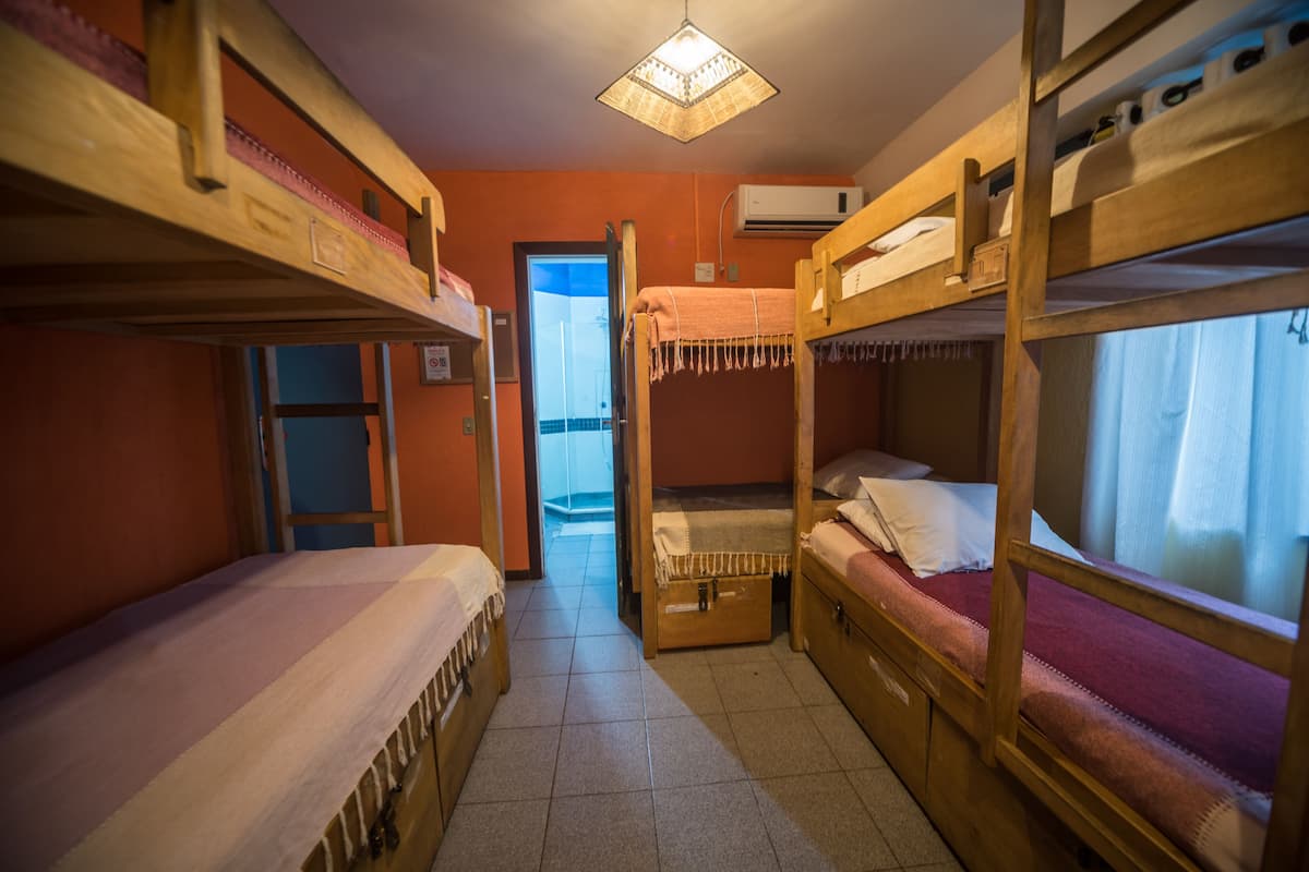 A dormitory room with bunk beds, a door leading to another room, and an air conditioning unit on the wall.