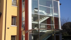 A modern building with a glass facade, a red and yellow exterior, and a visible staircase leading to an upper floor.