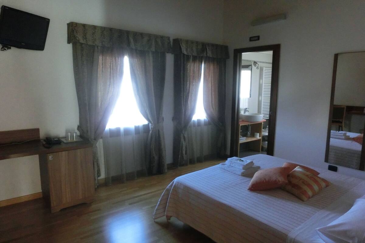 A hotel room with a wooden desk, a bed with pillows, and a bathroom visible through an open door.