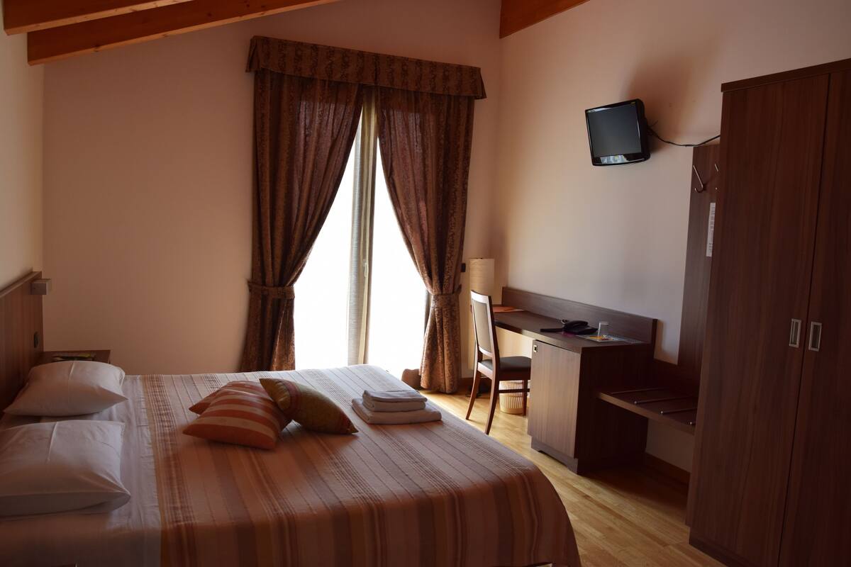 A hotel room with a bed, a desk, a television, and a wardrobe.