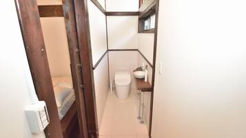 A narrow bathroom with a toilet, sink, and a small window.