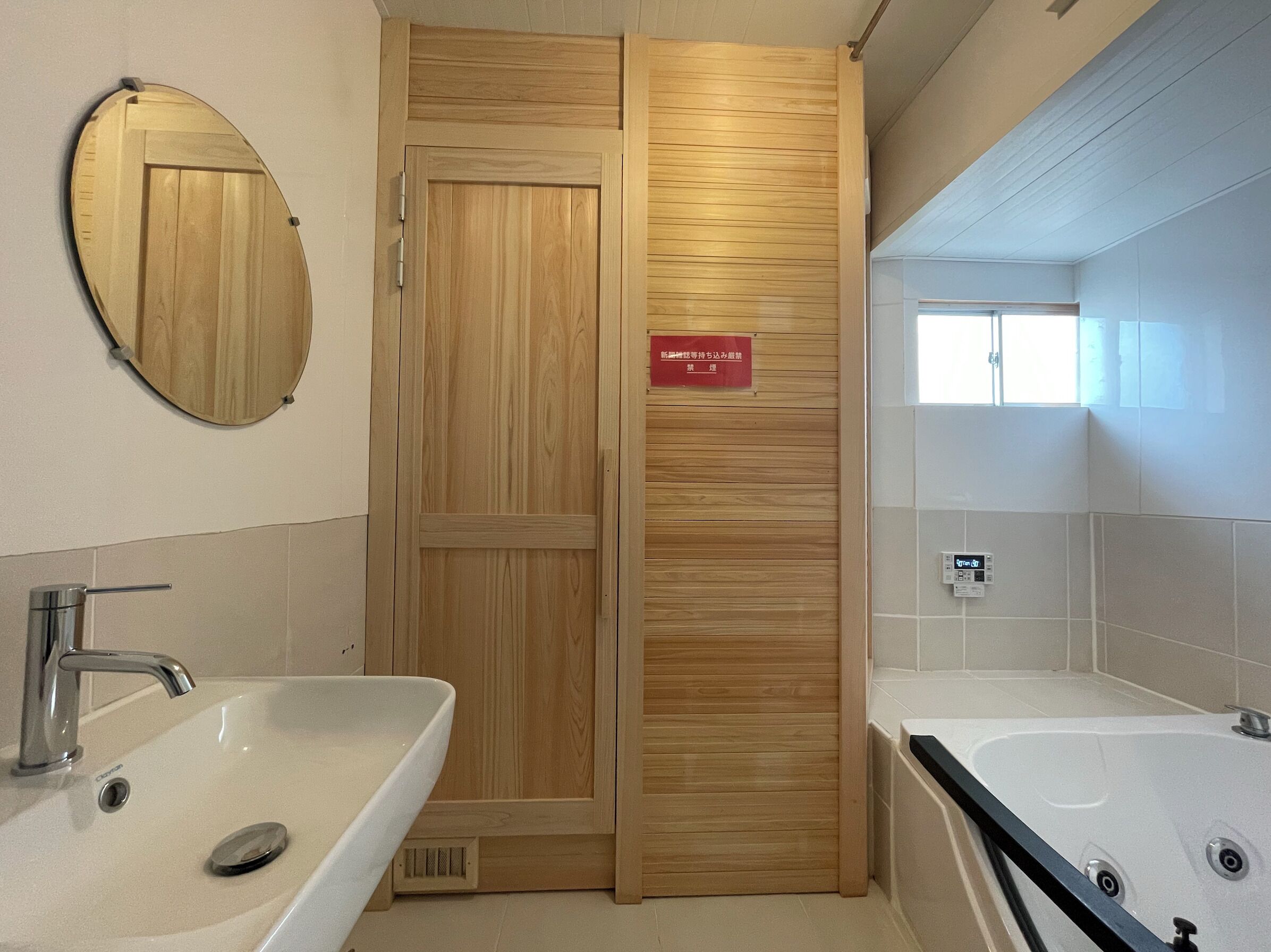 A modern bathroom with two sinks, a large mirror, and a wooden door with a sign.