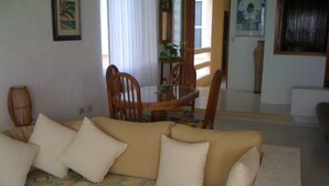Un saló amb un sofà, coixins, un llençol estampat, una taula de dinar amb cadires, i una vista de la zona de dinar.