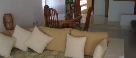 Una sala de estar con un sofá, almohadas, un plaid estampado, una mesa de comedor con sillas y vistas al área de comedor.