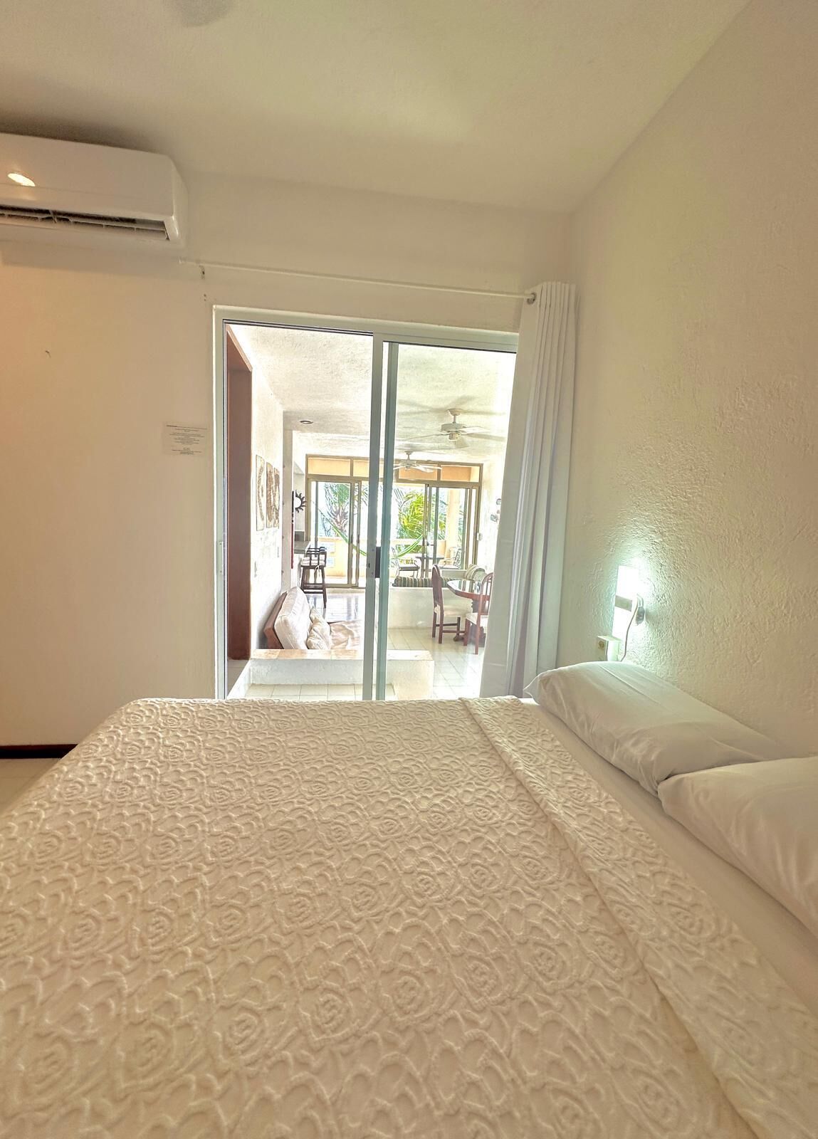 Ein Hotelzimmer mit Bett, Deckenventilator und Blick auf den Außenbereich durch eine Schiebetür.