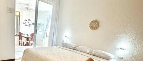 Quarto com uma cama grande, um ventilador de teto, uma mesinha e uma cadeira.