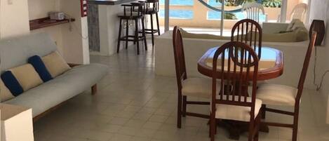 A living room with a sofa, dining table with chairs, and a view of the ocean through large windows.