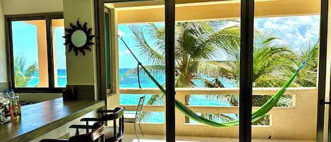 Una habitación con un amplio ventanal corredero que da a un balcón con vista al océano y palmeras.