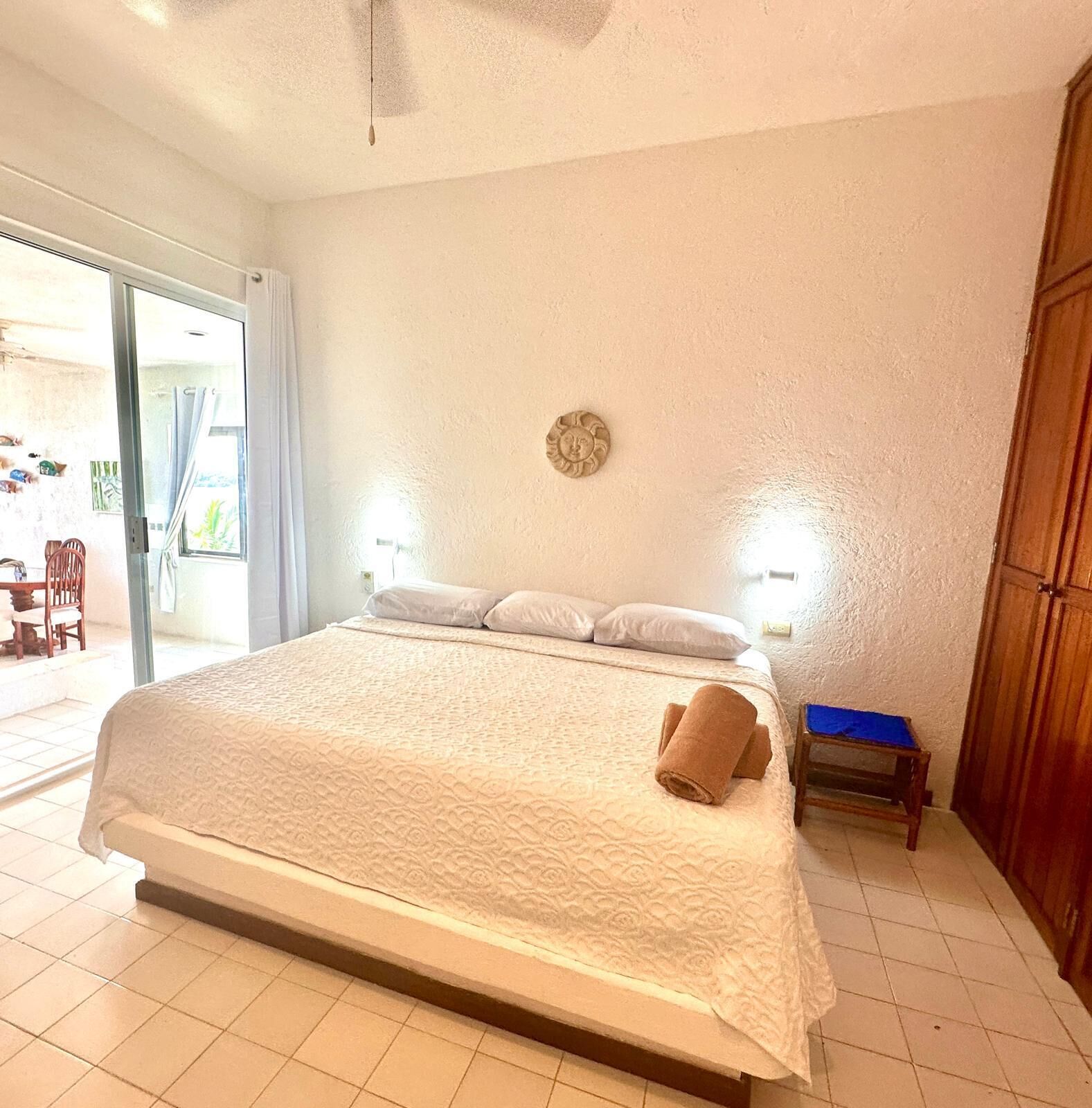 Une chambre spacieuse avec un grand lit, une table de chevet en bois et une vue sur l’extérieur grâce à une porte-fenêtre coulissante.